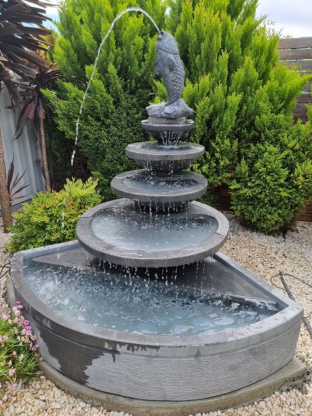 Large five tier corner unit with spitting fish in garden with large green plants