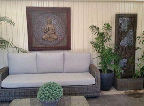A comfy outdoor sitting area with sofa, Buddha panel on the wall and a wall water feature with silver fisf.