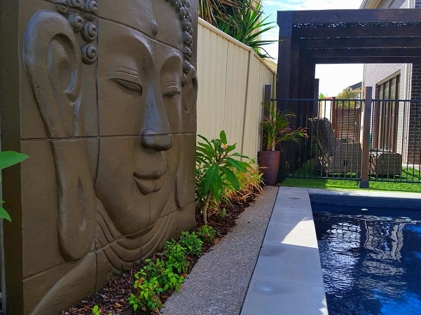 A large Buddha panel nestled into a narrow garden next to a swimming pool