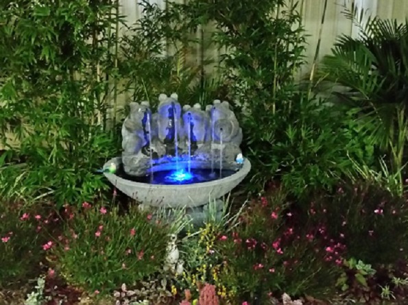 Water Feature with four frogs sitting on a bowl on a lovely garden at night with a blue light in the pond.