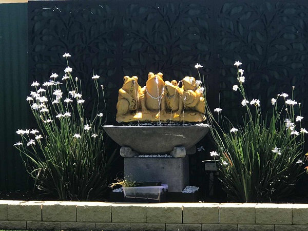 Water feature with four frogs painted gold and sitting on a bowl amongst white flowers