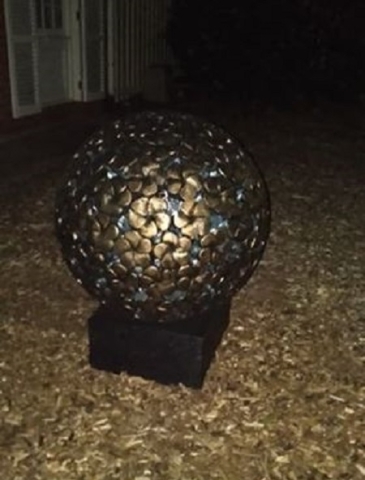 Round ball of carved frangipanis painted bronze with a light in it at night.