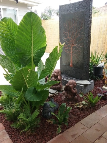 Wall water feature with decorative copper panel in a garden bed with plants and monks.