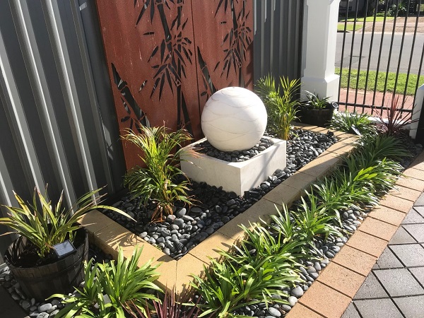 White ball water feature with decorative rust panels behind it and surrounded by plants