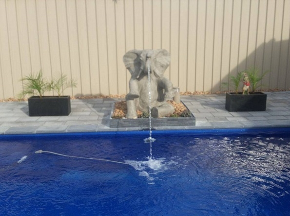 Sitting elephant statue next to swimming pool with water coming out of his truck into the pool